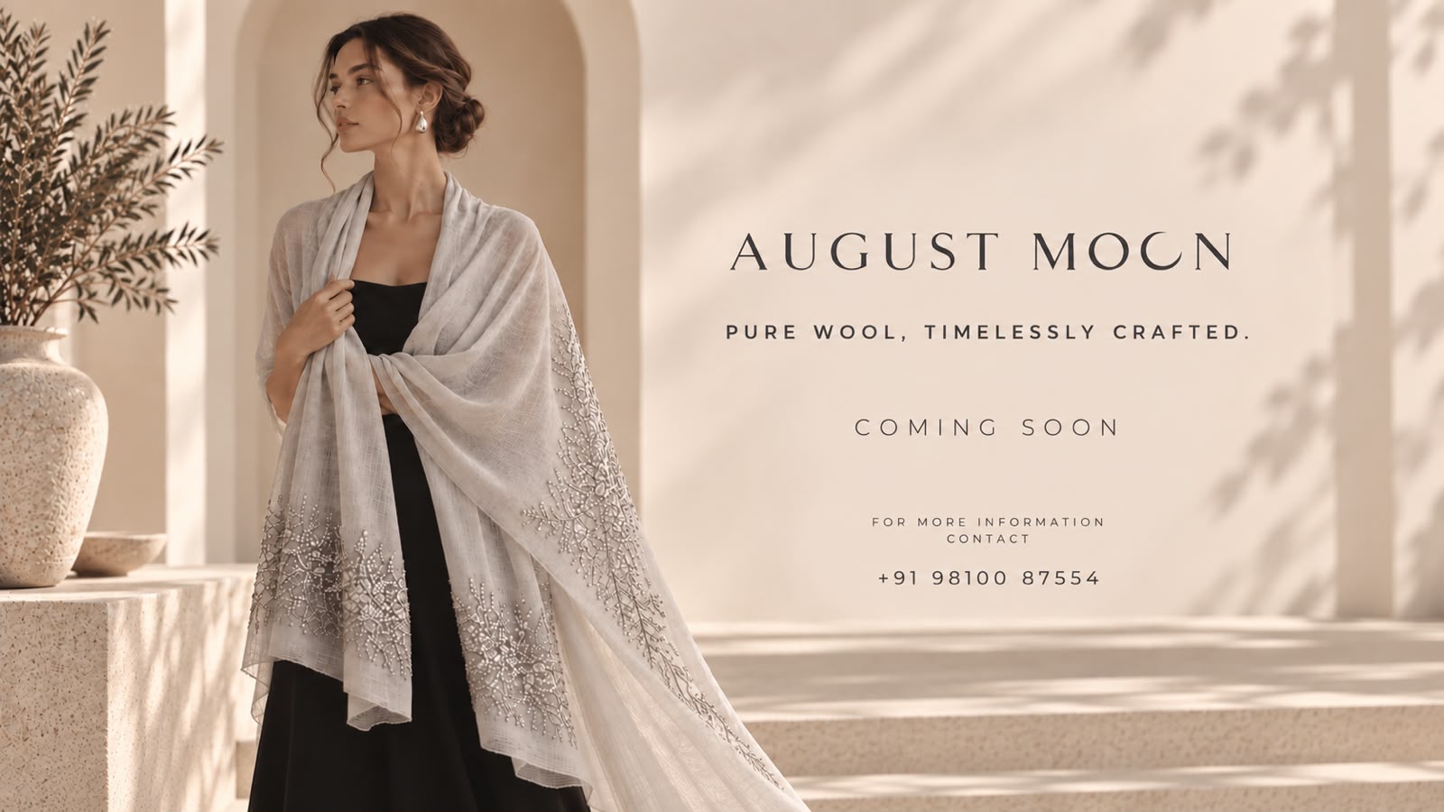 Woman wearing a pale grey pure wool August Moon shawl with hand-embellished floral embroidery, over a black gown